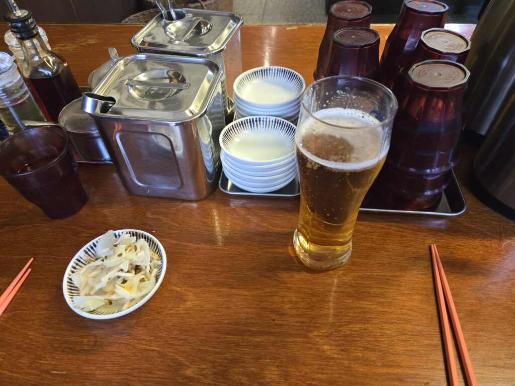 A refreshing glass of draft beer served with a side of pickled ginger and radish at Kanda Soba, Busan.