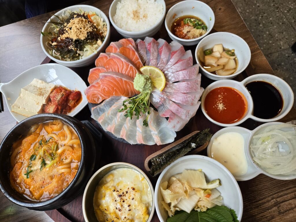 A full table setting with sashimi, corn cheese, and Kimchi Udon at Pado Busan